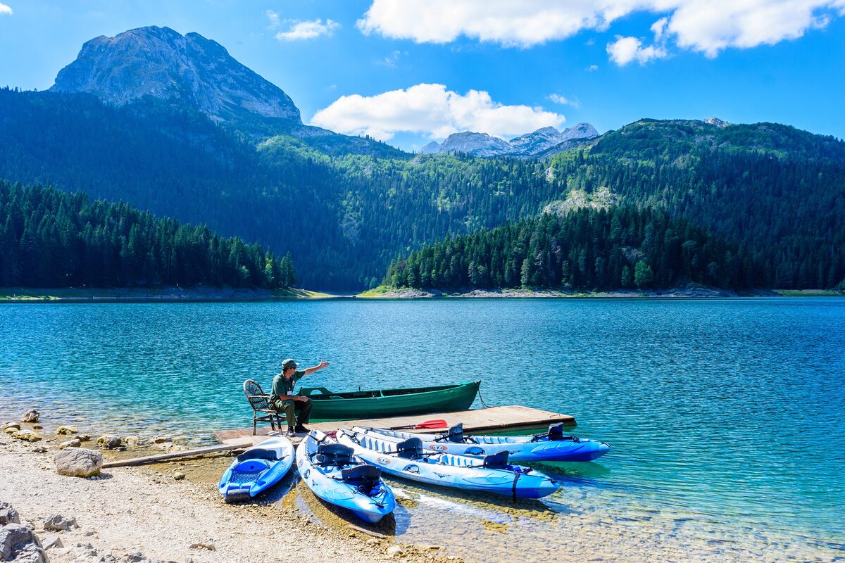 The Black Lake in Durmitor National Park: turquoise water with kayaks and a rowing boat at a small jetty, and forested slopes with a rocky peak behind