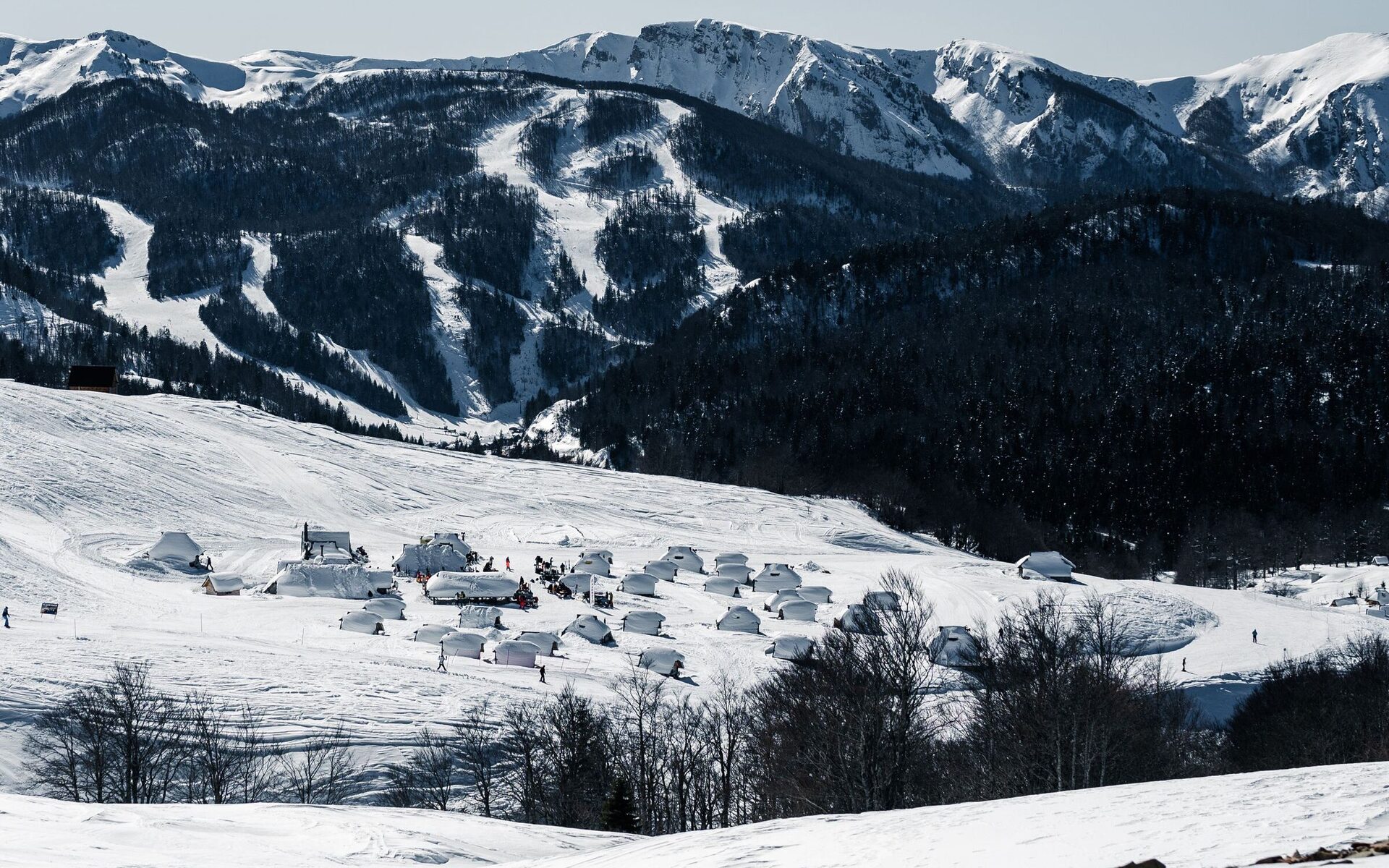 Snow-covered mountains near Kolašin in winter, with ski runs cutting through the dark forest above a hamlet of huts on a white hillside