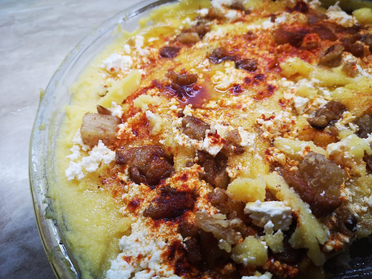 Baked kačamak: cornmeal and potato mash under melted cheese, with pieces of smoked meat scattered on top