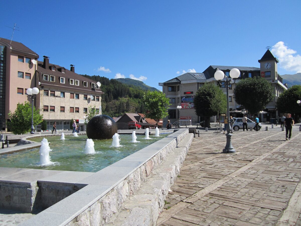 The main square of Kolašin in summer, with a stone fountain and town buildings behind it