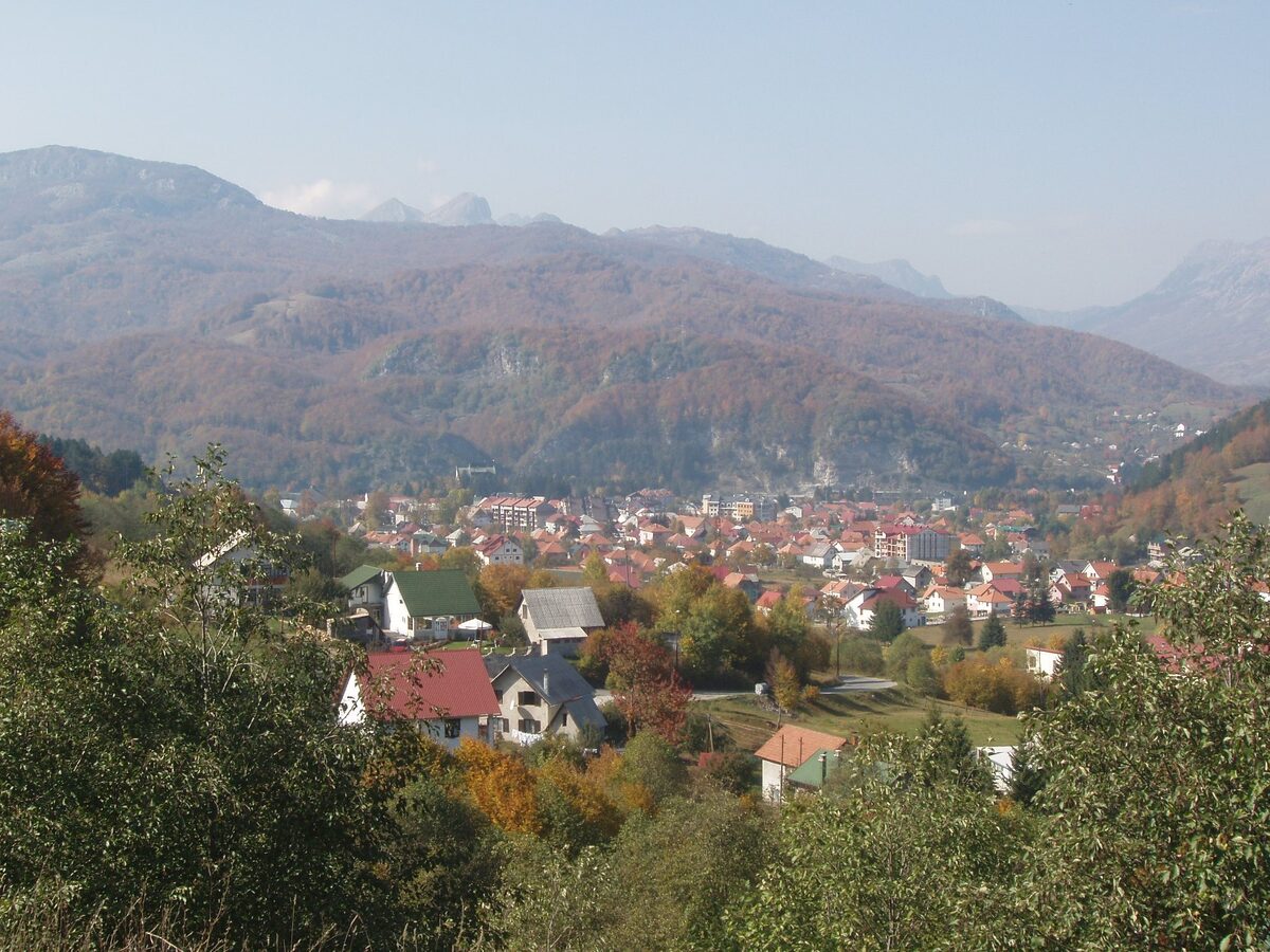 The town of Kolašin seen from a hillside in autumn, with red-roofed houses in the valley and forested mountains behind