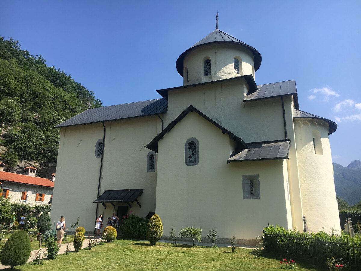 Morača Monastery in early summer: the white church with its dome and dark roofs under a blue sky