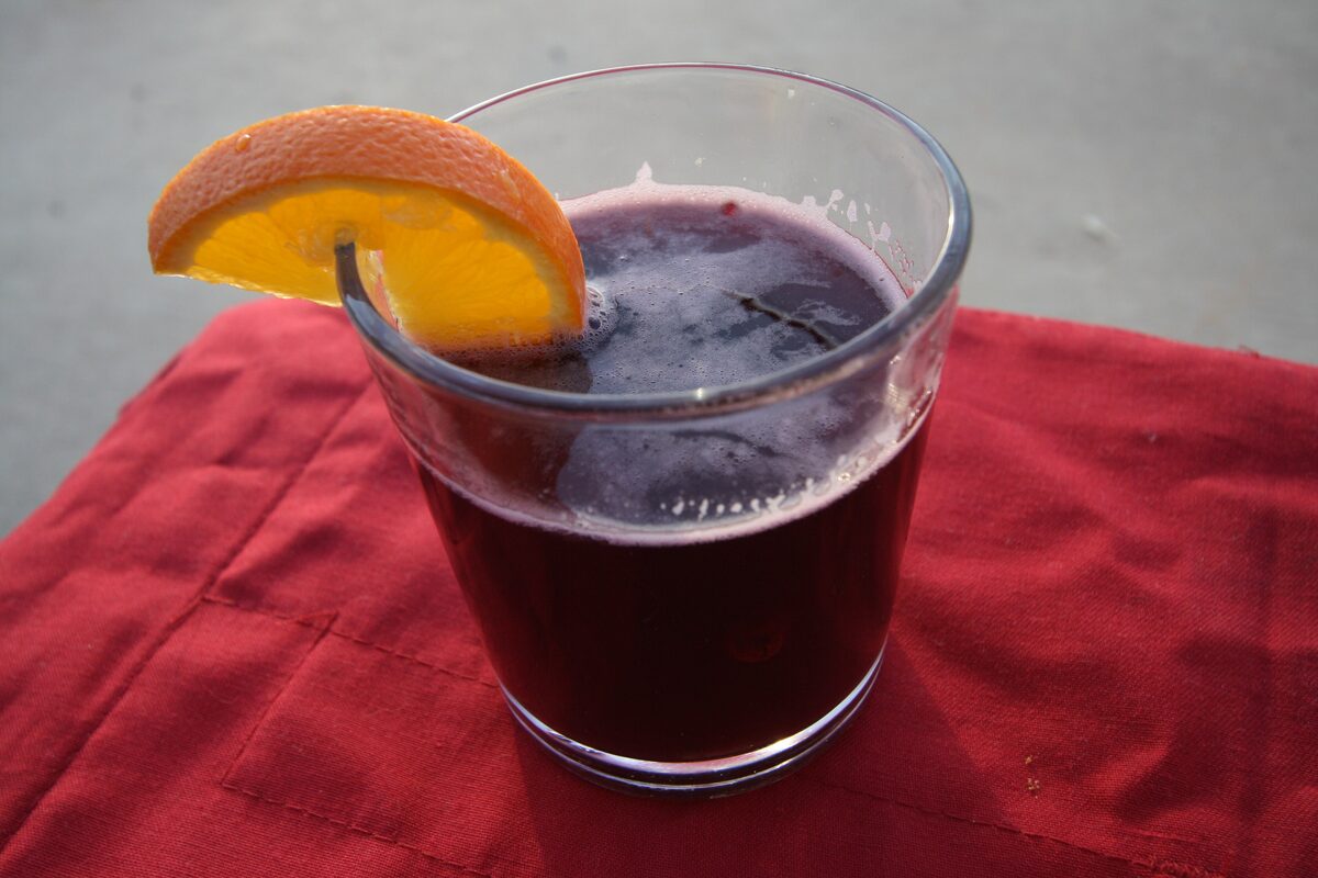 A glass of hot mulled wine with an orange slice on its rim, standing on a red cloth