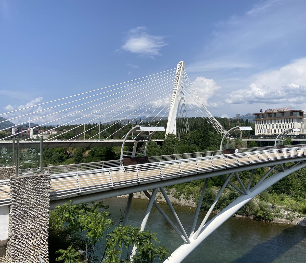 The Millennium Bridge over the Morača river in Podgorica: a white cable-stayed bridge with the river below and city buildings behind it