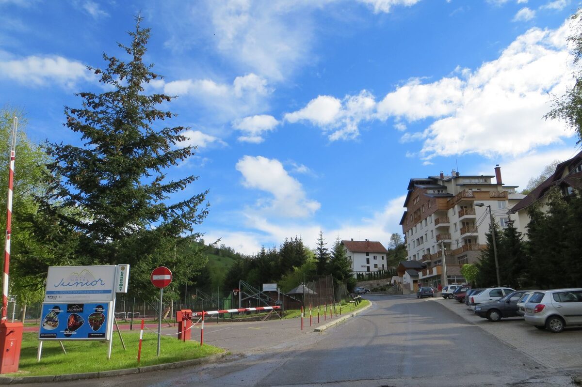 The road into Brzeće past the national park fee ramp, with hotels and apartment buildings and spruce trees under a blue sky (summer photo)