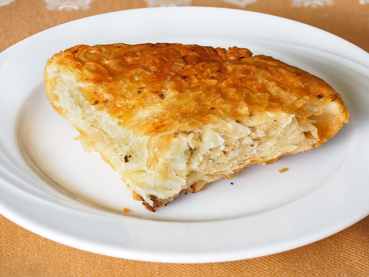 A slice of golden flaky burek on a white plate