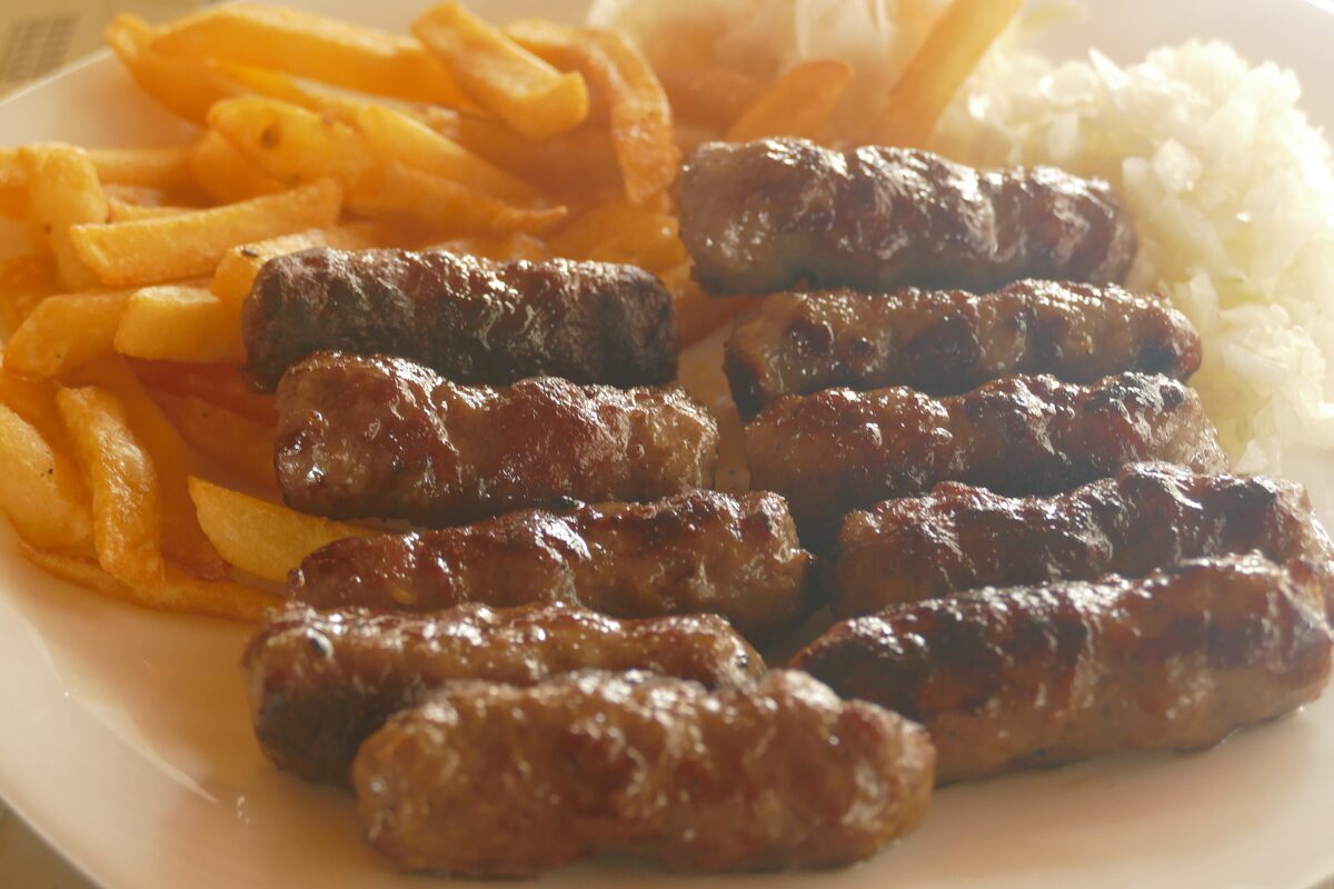 A plate of grilled ćevapi with french fries and chopped raw onion