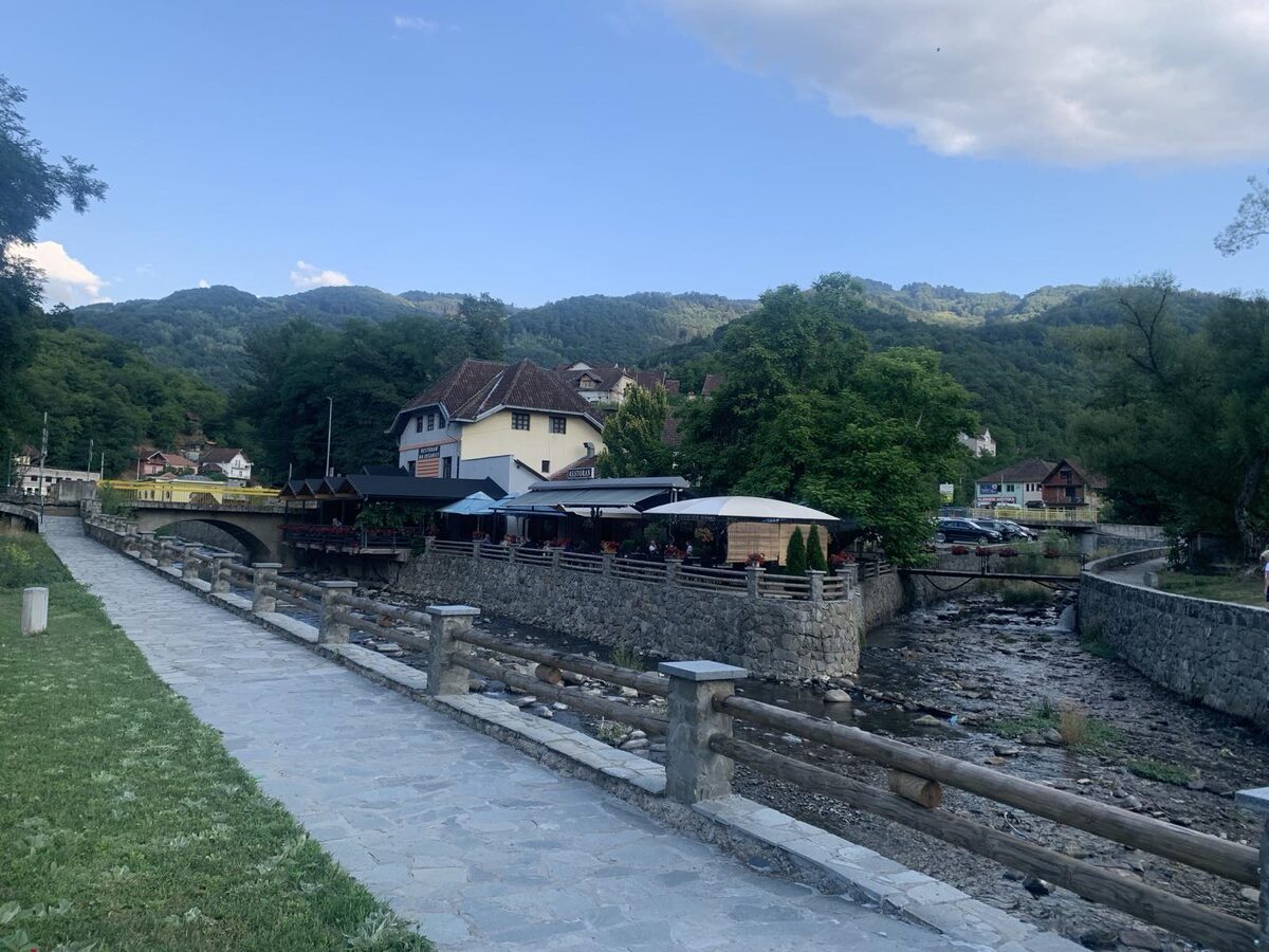 The stone-walled river promenade in Jošanička Banja, with café terraces and wooded hills behind