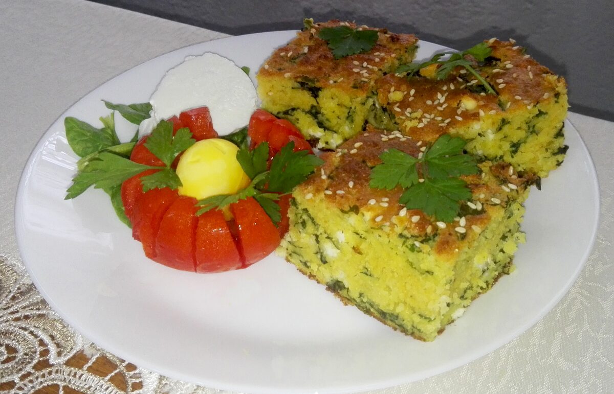Squares of baked cornbread with spinach and cheese, topped with sesame seeds (a Macedonian version of proja), on a white plate
