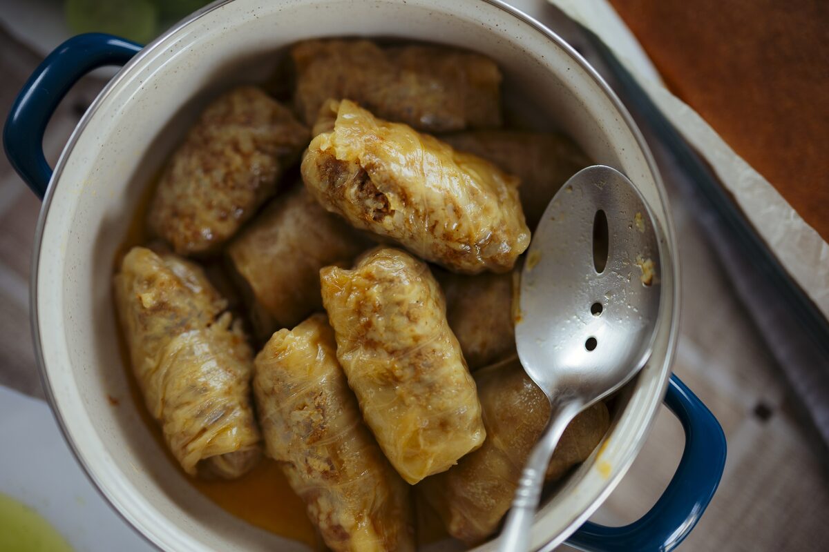 Cabbage rolls (sarma) in a white enamel pot with a slotted spoon