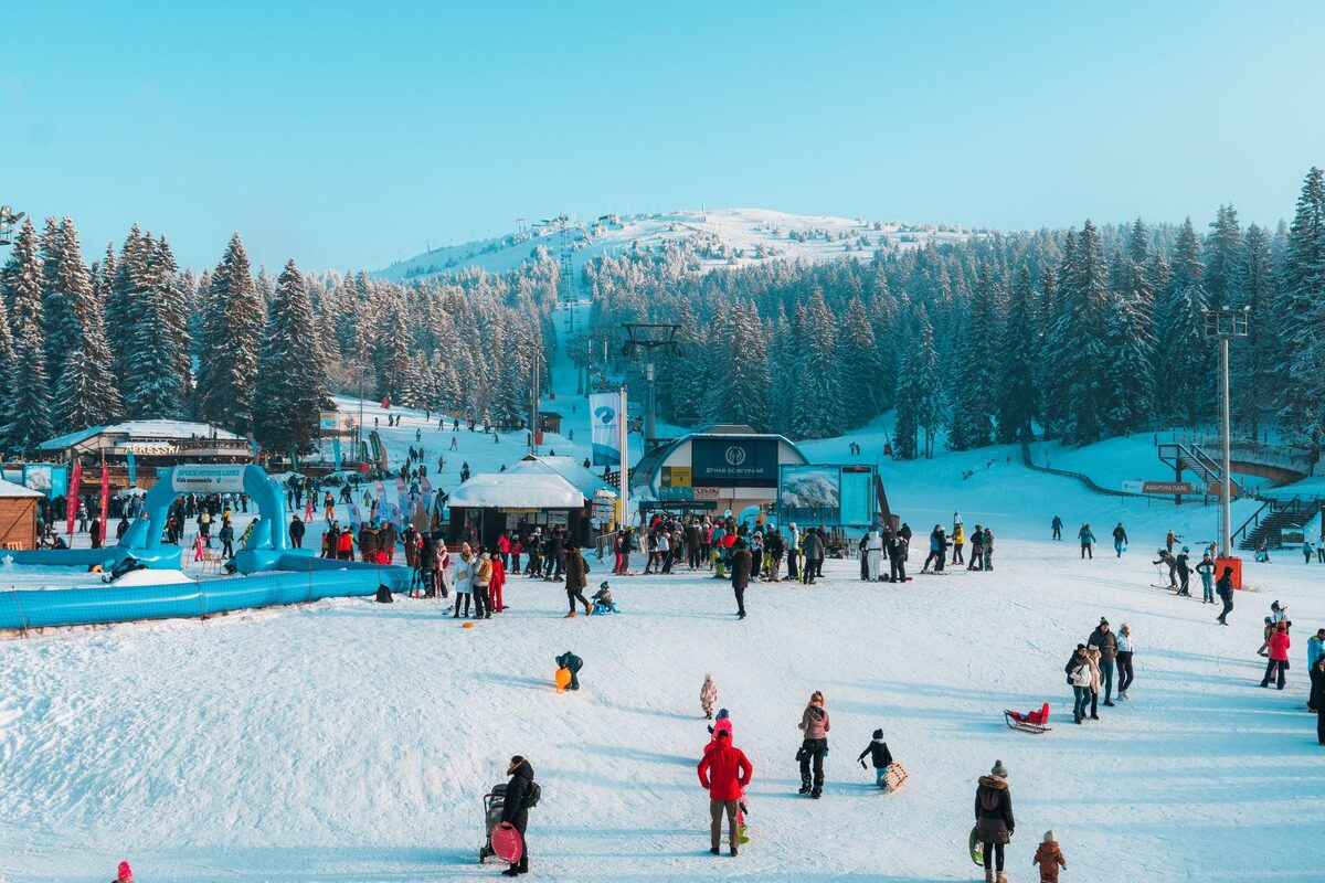 Families sledding and playing in the snow at the foot of a chairlift under a clear blue sky