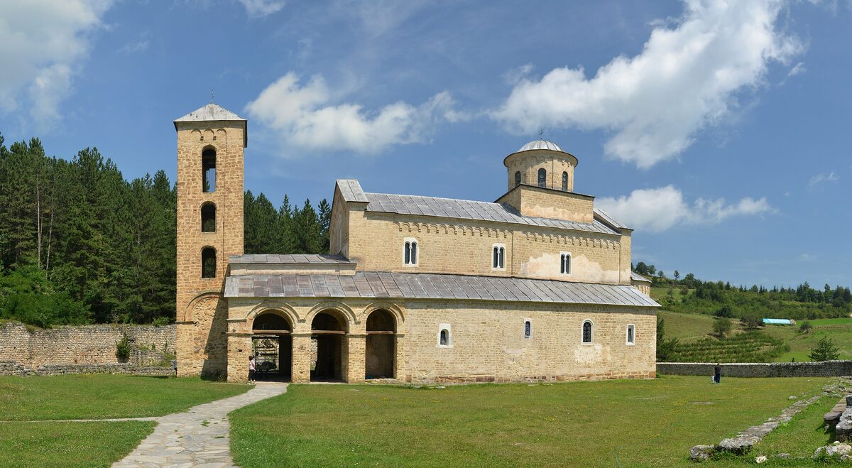 The stone church of Sopoćani Monastery with its bell tower and arched porch, on a lawn under a blue sky