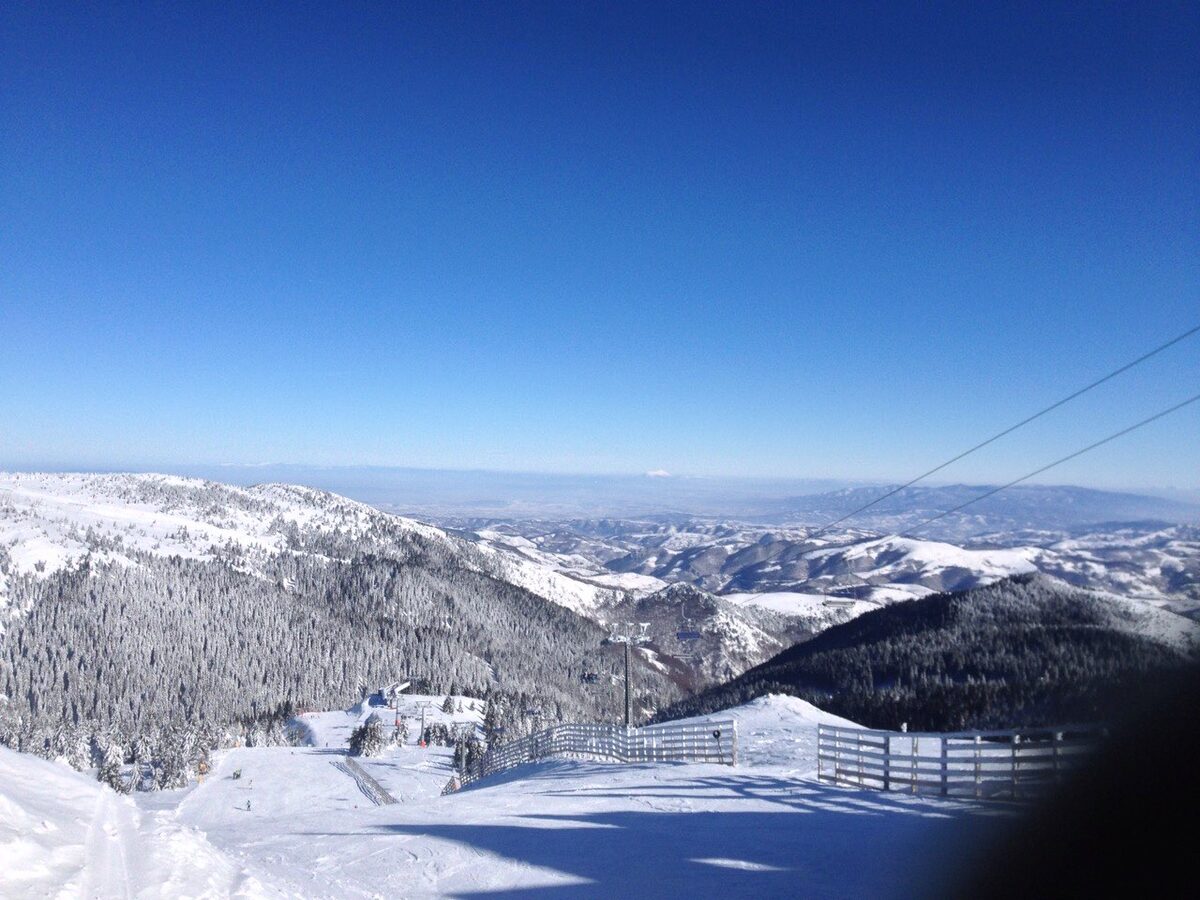 A groomed run with a chairlift above snowy forested ridges, looking out over the hills from the high plateau