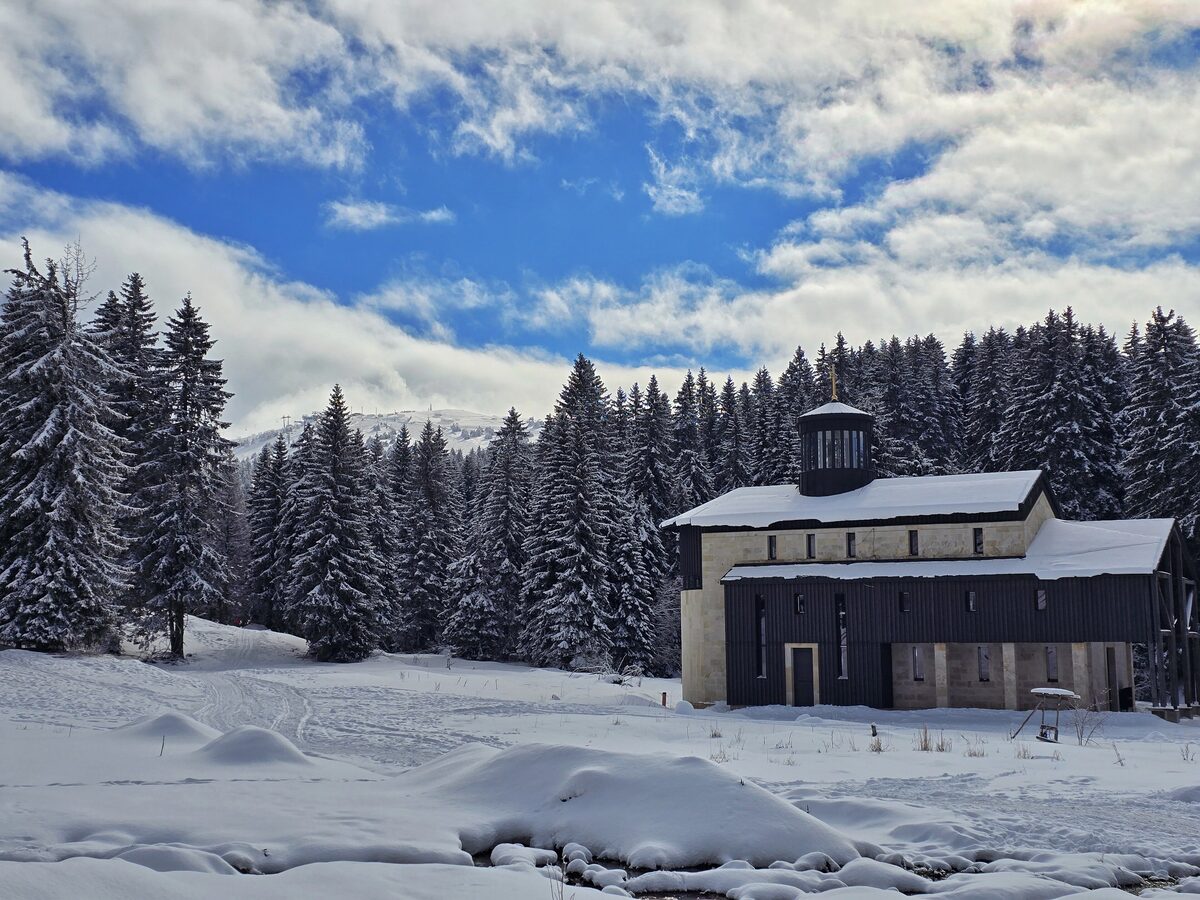 A modern stone-and-timber church with a small dome, deep in snow among spruce forest on Kopaonik