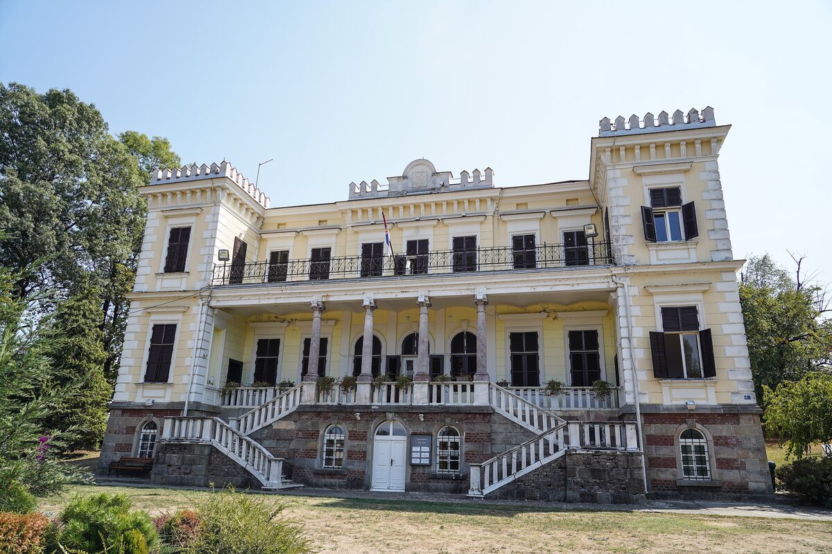 The yellow Belimarković castle in Vrnjačka Banja, with a double staircase and a flag on the balcony