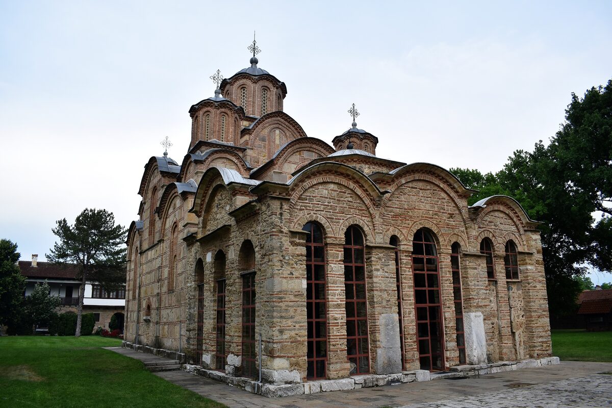 The Gračanica monastery church, its stone-and-brick walls rising in stepped arches to five domes, beside a lawn and monastery lodgings.