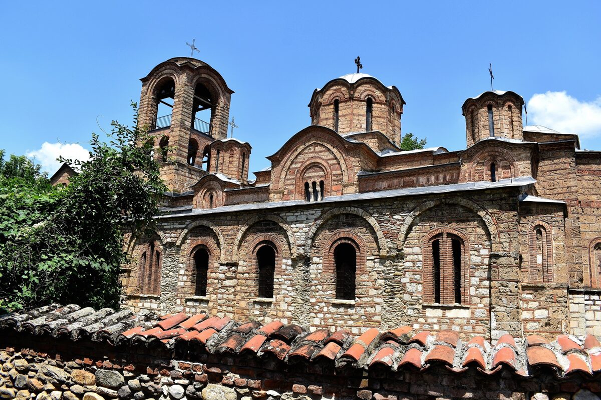 The stone-and-brick Bogorodica Ljeviška church in Prizren, with its bell tower and domes rising above a tiled garden wall.