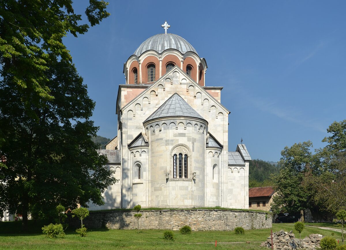 The white marble Church of the Virgin at Studenica monastery seen from the east, its apse and dome against a deep blue sky.