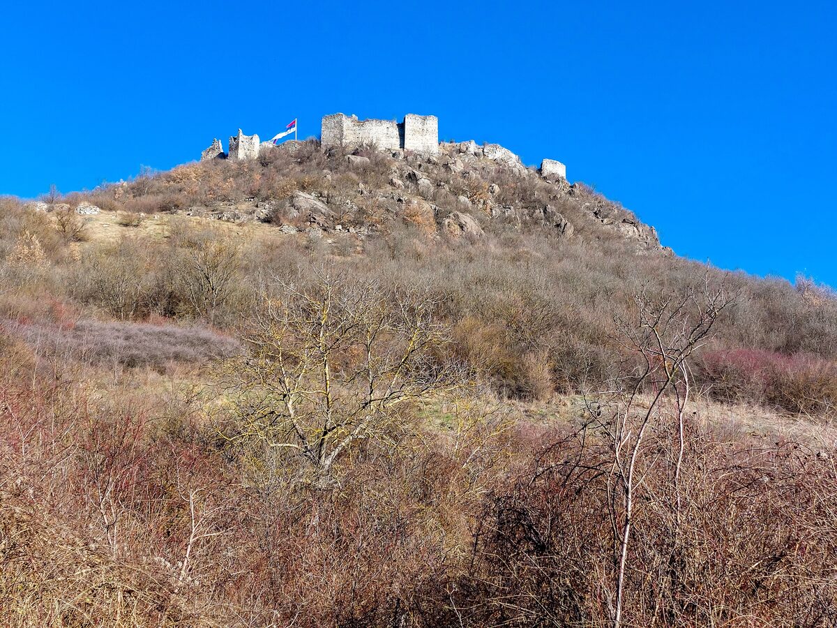 The ruined walls and towers of Zvečan fortress crowning a rocky, scrub-covered hill under a deep blue winter sky.