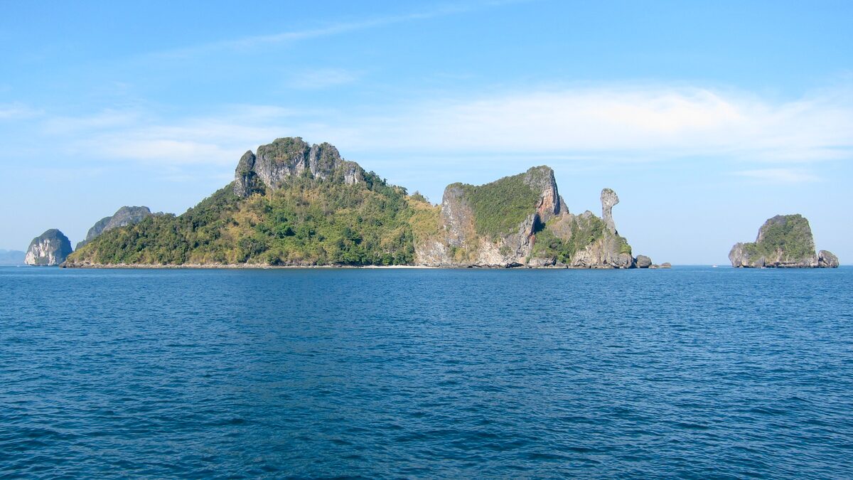 Wooded limestone islands seen across open blue sea, with a tall rock spire on the right