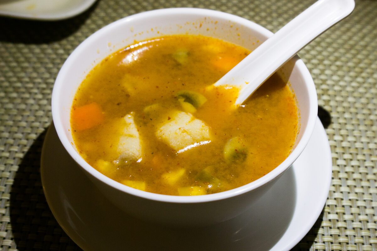 A bowl of yellow sour fish soup with chunks of white fish and vegetables
