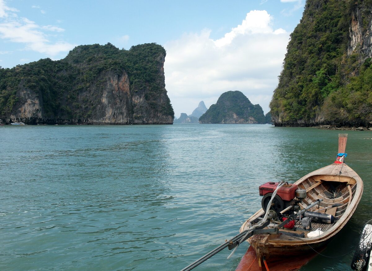 Bow of a longtail boat on calm green water between forested limestone cliffs at Koh Hong