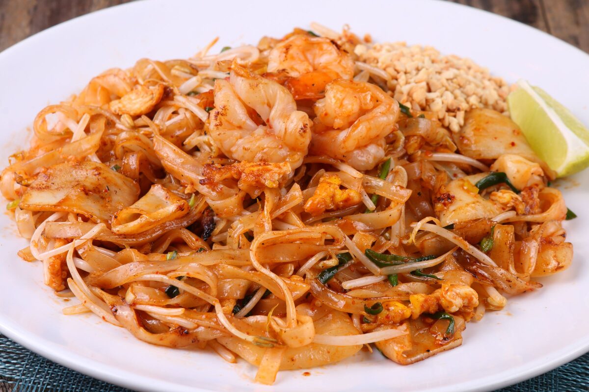Pad Thai with shrimp, egg, bean sprouts and crushed peanuts on a white plate, with a lime wedge