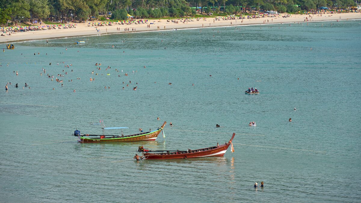 Swimmers and a few longtail boats in the bay at Kata Beach, Phuket, with trees along the shore