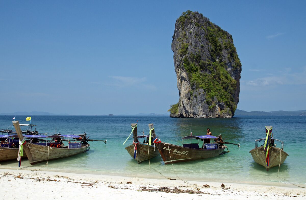 Three longtail boats moored on the white sand below a limestone pillar on Poda Island
