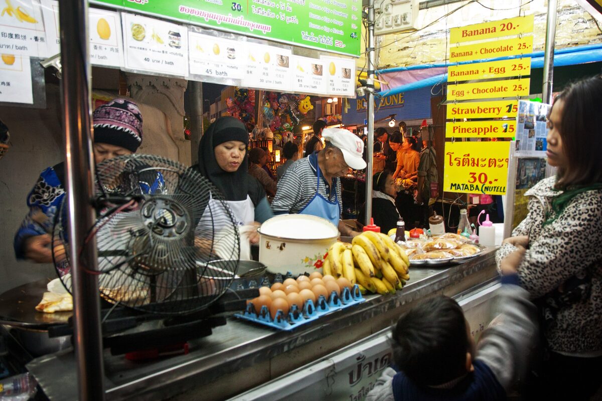 A street vendor cooking banana roti on a griddle at a stall