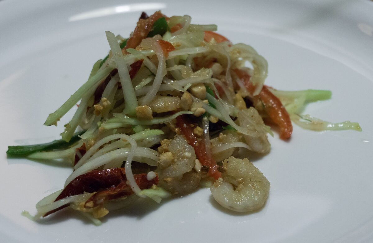 Green papaya salad with shrimp and chili on a white plate