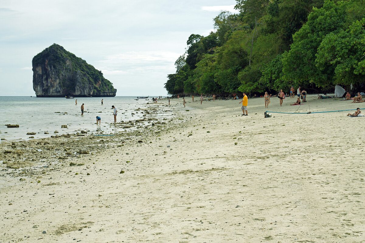 Low-tide beach on Ko Tup with a rocky islet on the left and people walking on the sand