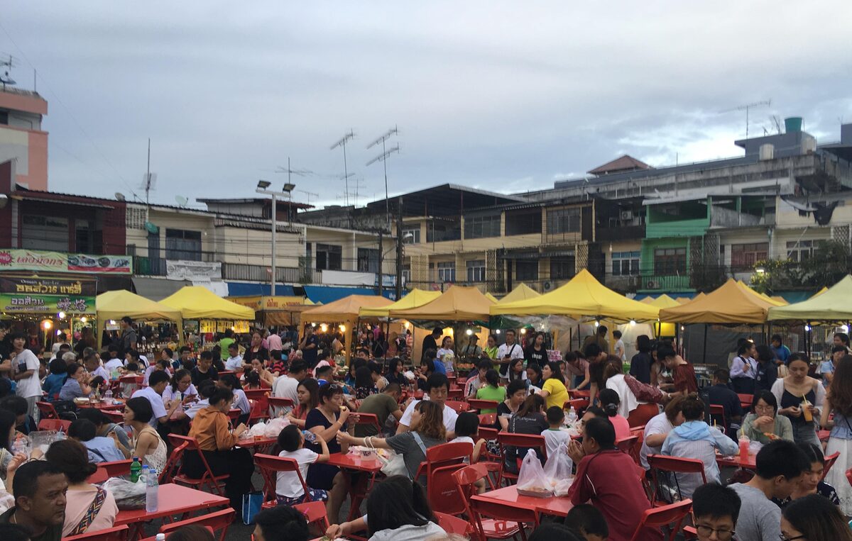 Crowds at the red plastic tables of the Krabi Town Walking Street market, with yellow awnings and shophouses behind