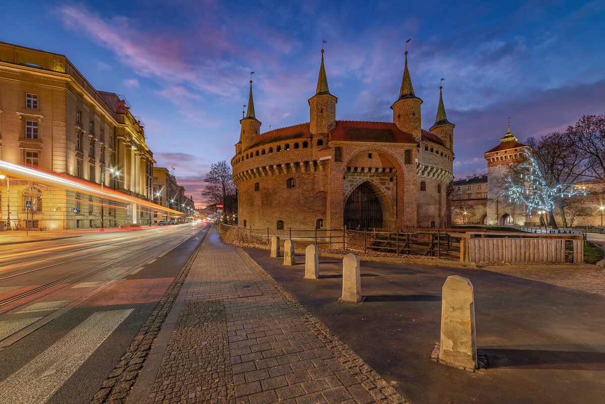The round brick Barbican with its seven turrets at dawn, next to a tram street with light trails