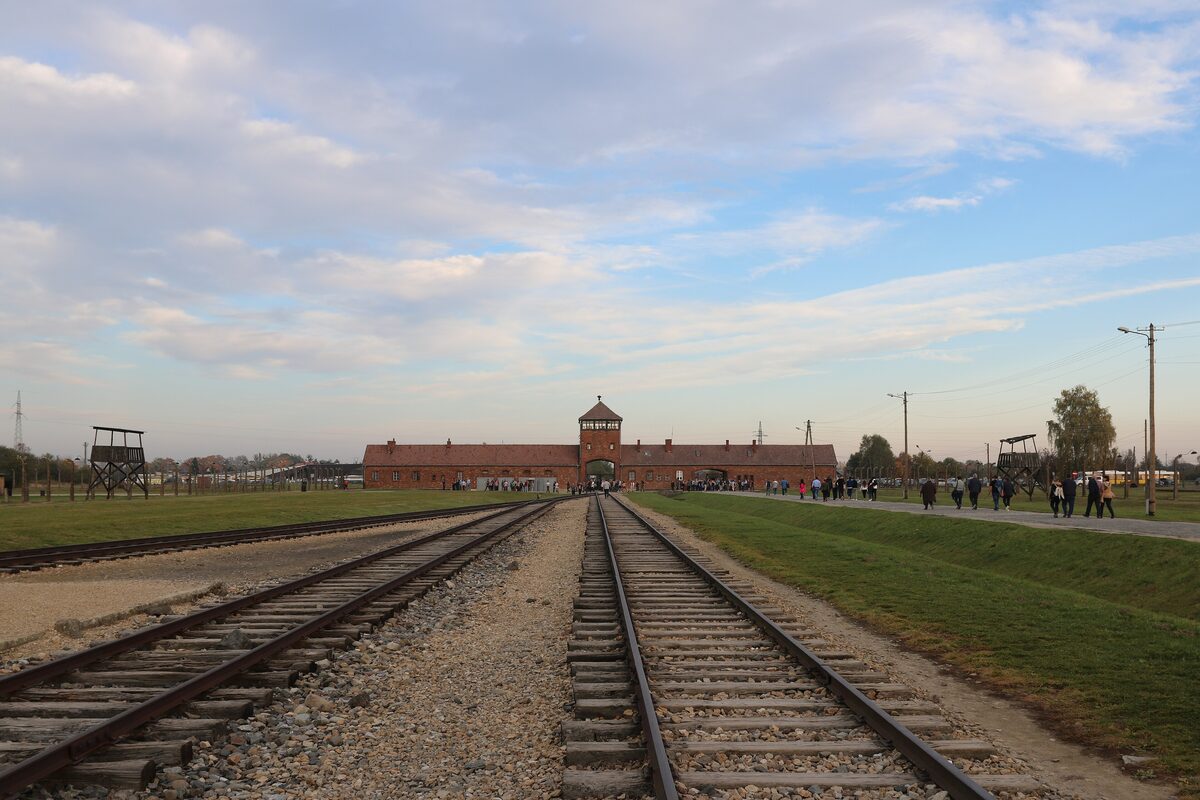 Railway tracks leading across the grass to the brick gatehouse of Auschwitz II-Birkenau
