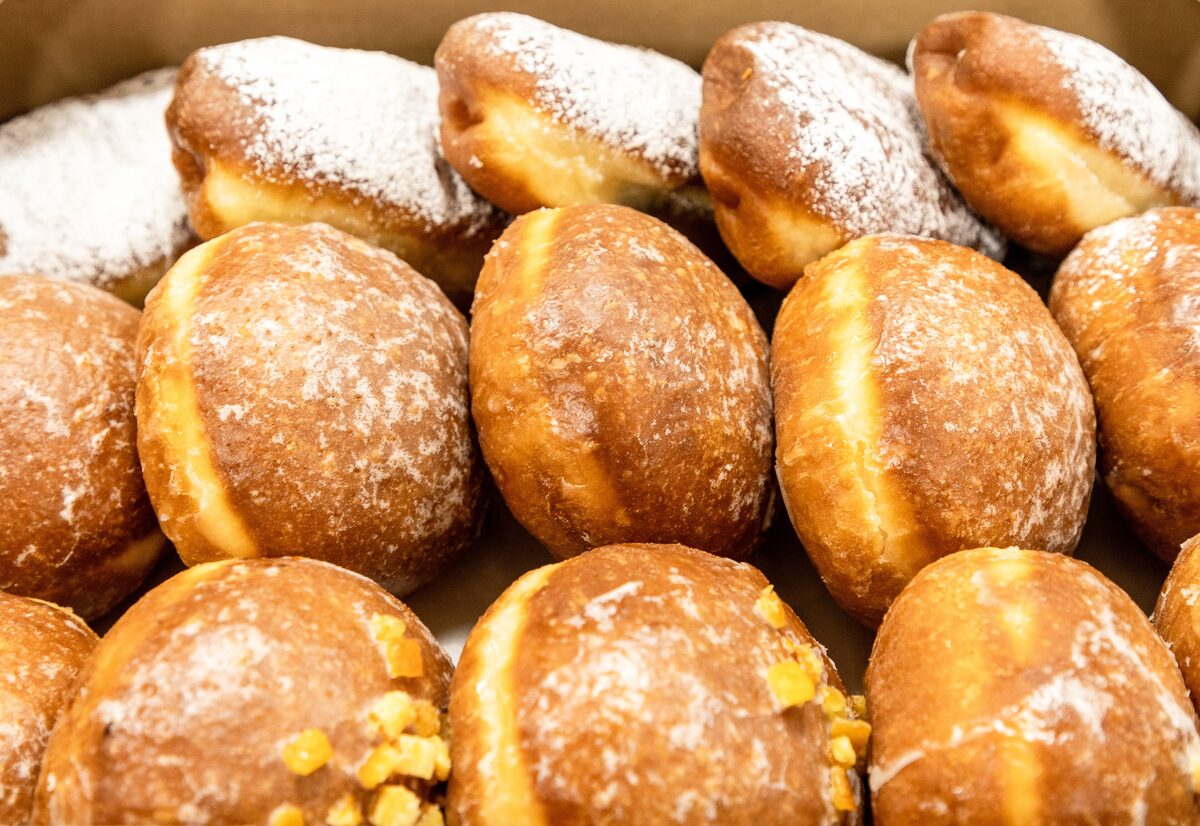A tray of Polish pączki doughnuts dusted with sugar, some showing their filling