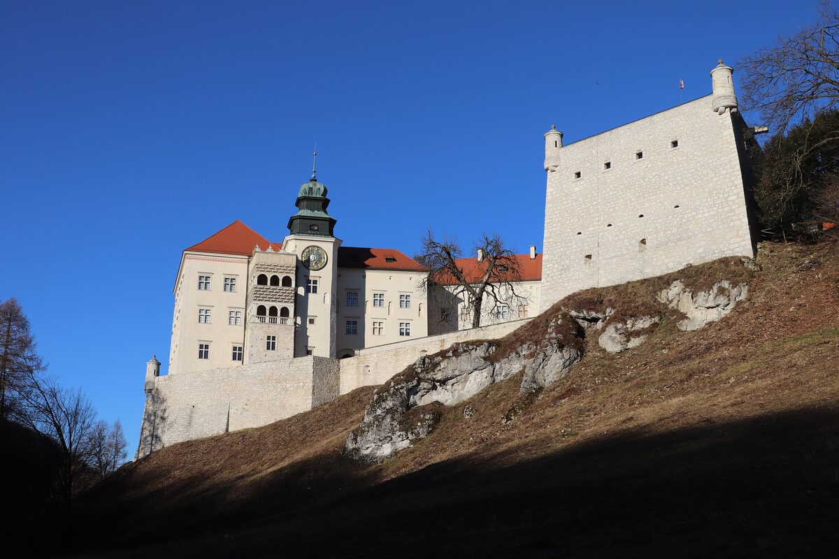 Pieskowa Skała castle with its white walls and clock tower on a rocky slope under a deep blue sky