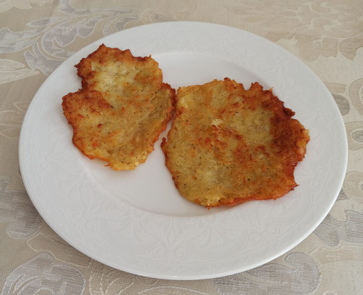 Two golden, crisp-edged potato pancakes on a white plate