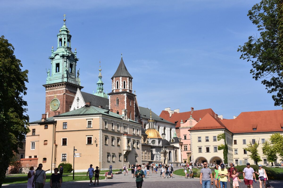 Visitors walking across the square on Wawel Hill toward the cathedral's clock tower and the castle buildings
