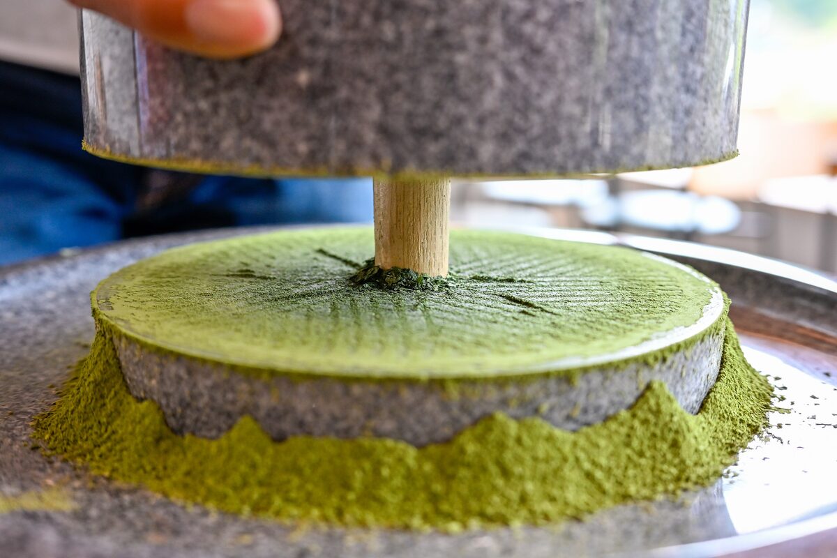 Bright green matcha powder piled around a granite stone mill with a wooden handle, as it is ground from tencha leaves in Uji