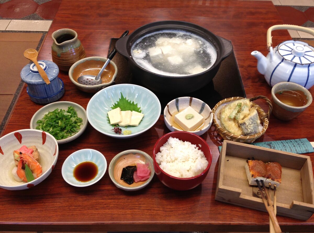 A yudofu meal with tofu simmering in a clay pot, surrounded by small side dishes and rice