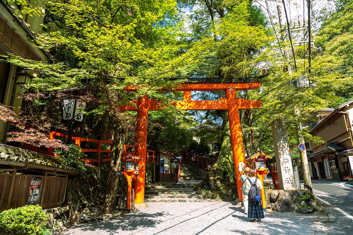 The vermilion torii gate and lantern-lined stairs of Kibune Shrine, framed by fresh green maples at the entrance to Kibune