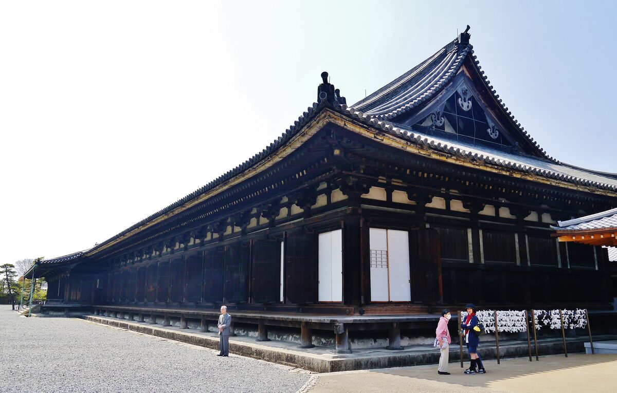 The long, low dark-wood main hall of Sanjusangen-do seen from its gravel yard, with a few visitors at the foot of the veranda