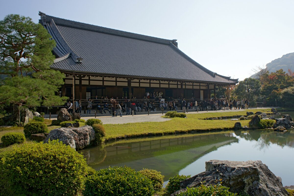 The grey-roofed main hall of Tenryu-ji across the still garden pond, with clipped shrubs and rocks in the foreground