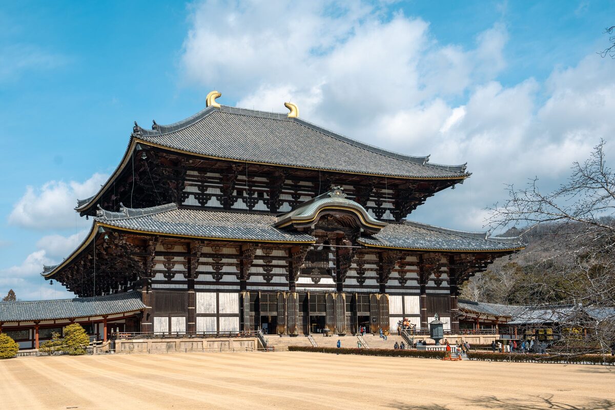 The Great Buddha Hall of Todai-ji, a vast dark-timbered double-roofed hall with gold ornaments on the ridge, across a sandy forecourt