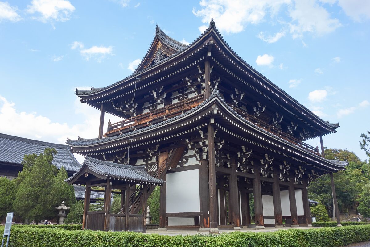 The two-storey main gate of Tofuku-ji with its tiled roof and carved brackets, under a blue sky