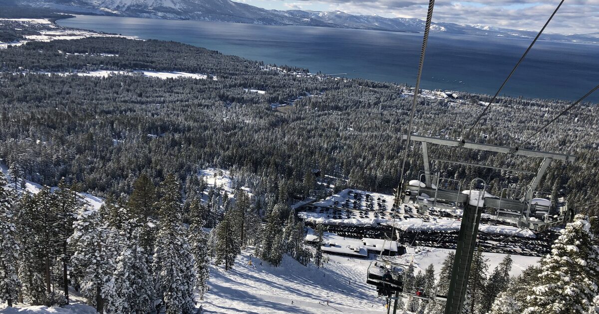 A chairlift above Heavenly's snow-covered runs, with pines below and Lake Tahoe and its snowy ridges beyond