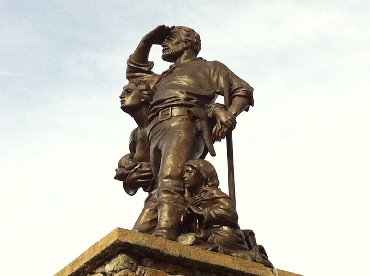 The bronze Donner Party pioneer statue, a man shading his eyes beside a family, against a pale sky