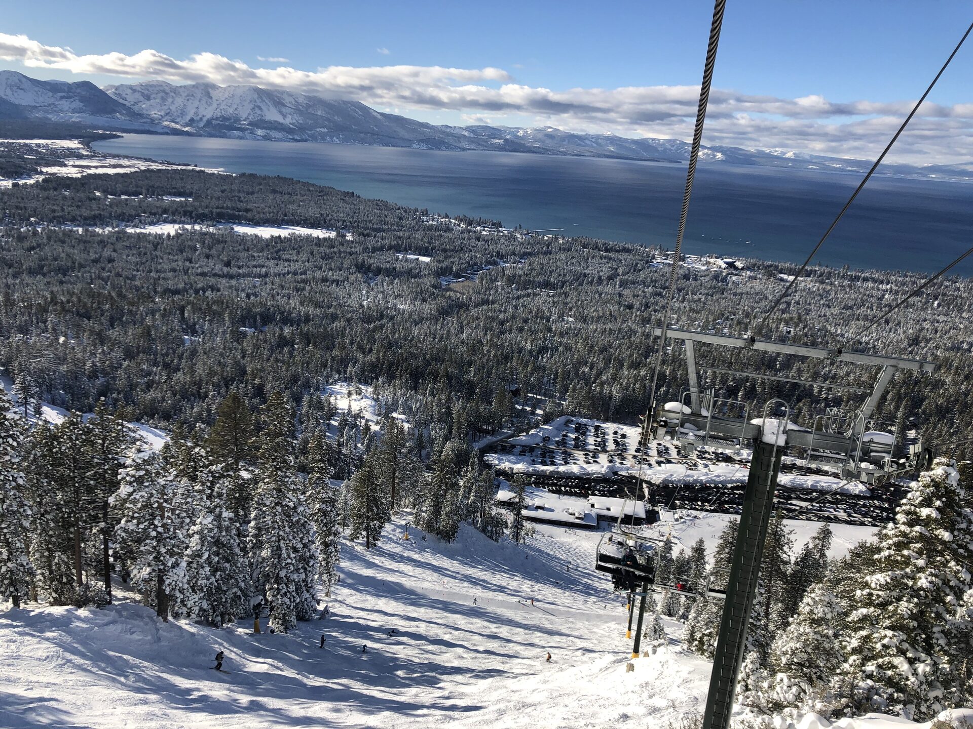 A chairlift above Heavenly's snow-covered runs, with pines below and Lake Tahoe and its snowy ridges beyond