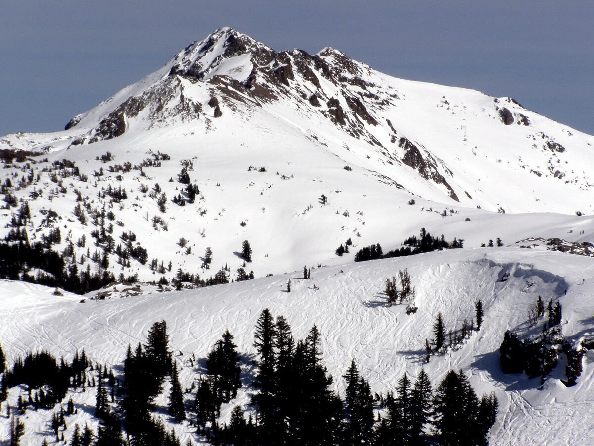 A rocky, snow-covered peak above a bowl of ski runs on the back side of Kirkwood, under a dark sky